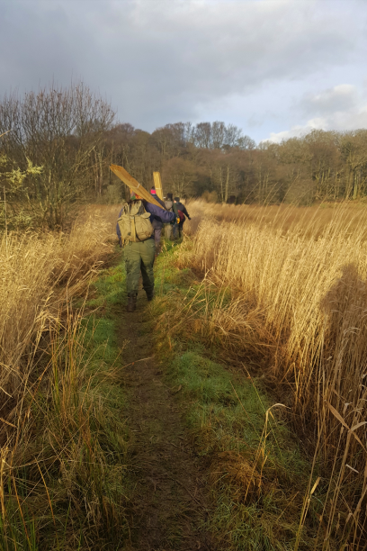 RSPB staff crossing the fen carrying equipment 