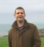 Jon Andrews pictured in one of the fields on his family farm, with the South Devon coastline, sea and sky behind him