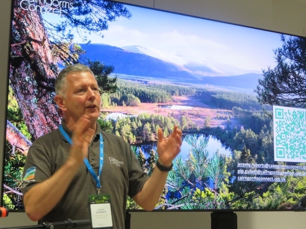 A person standing in front of a screen that is displaying an image of the Cairngorms