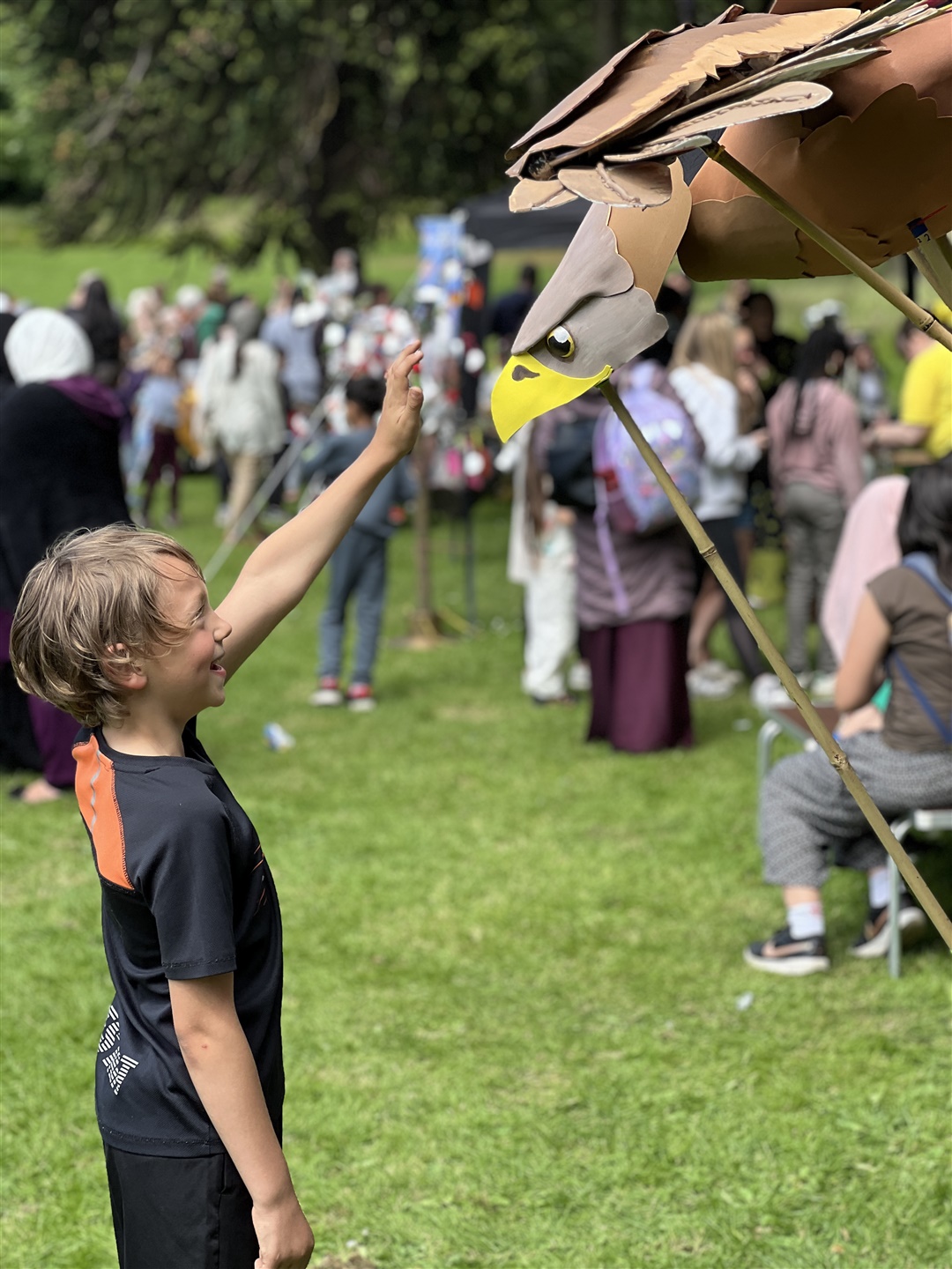 A young boy is reaching out to touch a model White-tailed Eagle in a park.