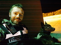 Russell sits on left of image in Police Unifrom with one hand on the shoulder of a dog