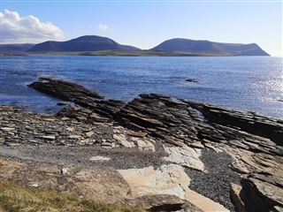 Stony shore with beautiful view across the sea on a sunny day. Hoy hills in the background