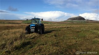 tractor mowing rush with snow capped Slemish mountain in the background