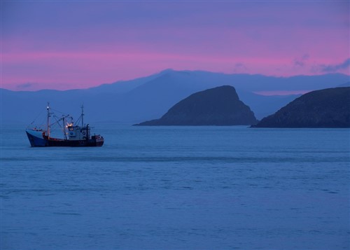 A boat with rocky islands behind with a stunning pinky purple sky