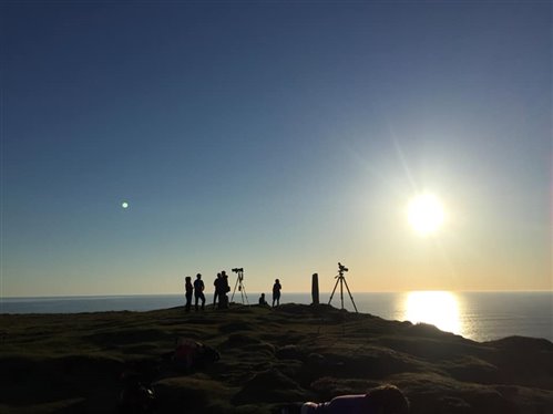 group of people stand at edge of cliff with wildlife watching equipment