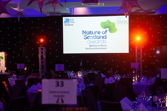 Image of tables set up for dinner with nature of scotland logo projected on screen