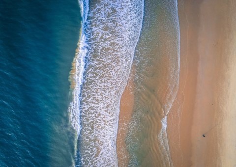 Aerial view of a golden sandy beach with waves breaking on the shore.