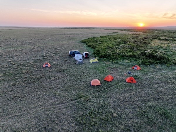 A drone image of a small camp on a grassy area, the sun is setting on the horizon