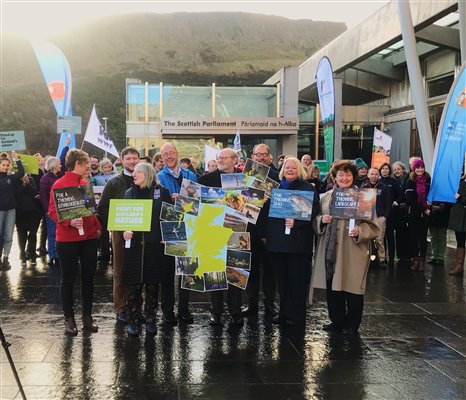 group of people gathered outside scottish parliament with environment link slogan placards