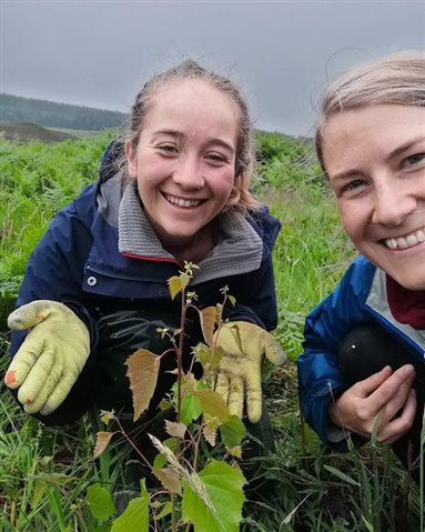 Two volunteers holding a small sapling tree out on the bog.