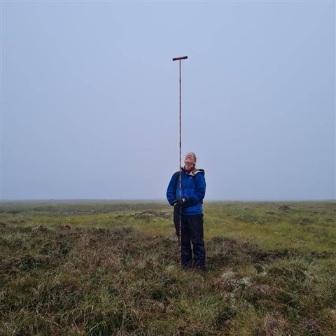 A volunteer holding a long pole which is drilled into the ground.