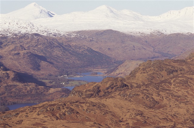 A birds eye view of Loch Lomond and the Trossachs National Park, with a series of mountains surrounding lochs in the valley floor. The mountains in the distance are covered in snow.