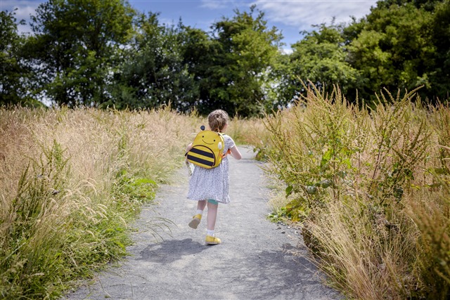 A young girl is walking down a path surrounded by tall grass and trees.