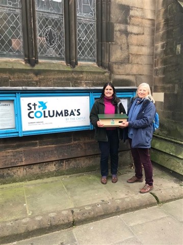 Two women holding a swift box next to St Columba's church.