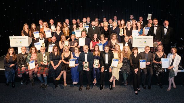 The Nature of Scotland Awards 2023 winners and highly commended on stage after the awards holding trophies and certificates.