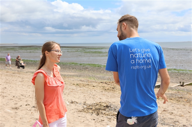 RSPB Scotland's David Hunt is conversing with an event attendee on a beach, with the sea in the background.
