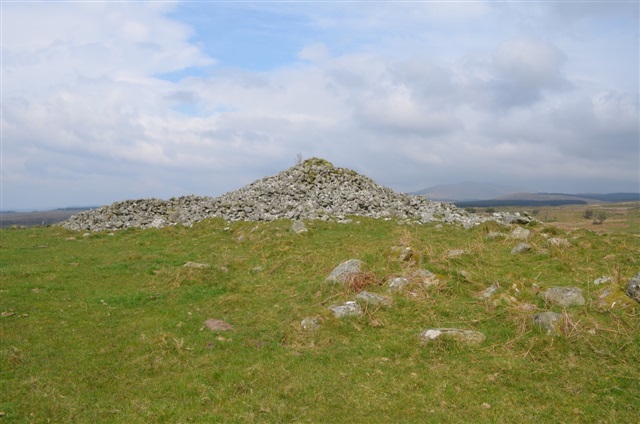  A three-metre high burial cairn is standing on a grassy field.