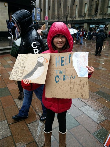 Sioned at a climate march. Her poster says "Stop yer huffin, save the puffin!"