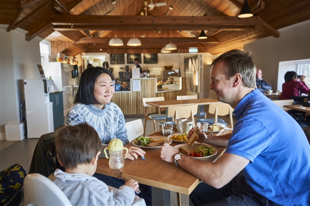A family of two adults and a child are sitting in the café at RSPB Scotland Loch Lomond. The two adults have a toastie and salad each while the child has some milk. 