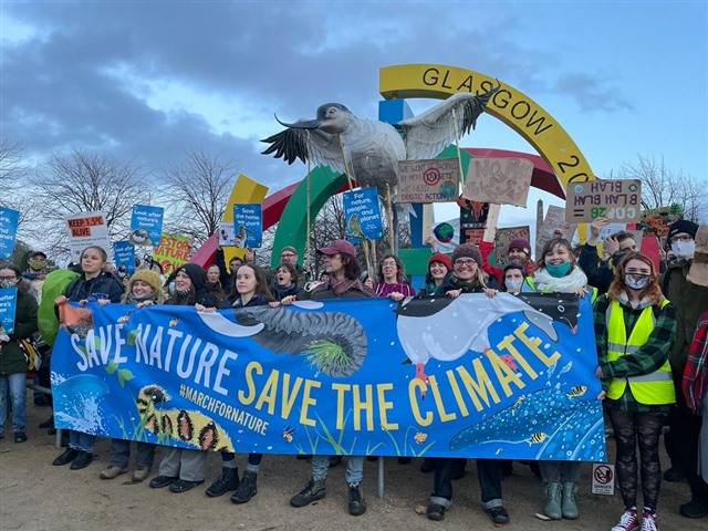 A group of people at the climate march holding posters and banners. The giant avocet puppet is above them, wings spread.