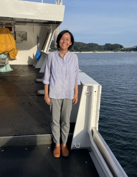 Person standing on the deck of a boat with land in the background